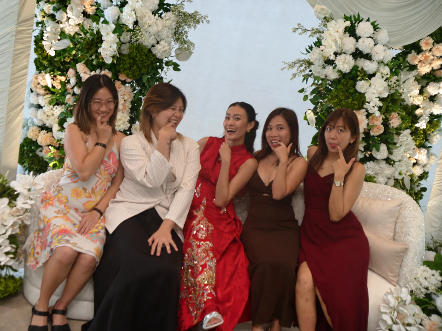 Five friends making playful faces together in front of the wedding flowers