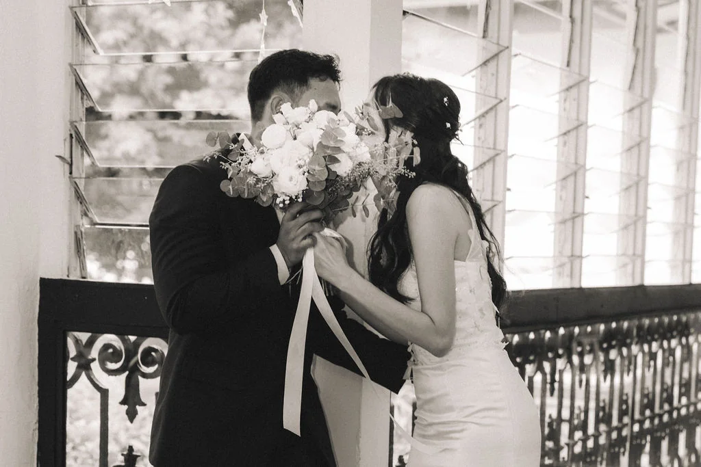 JR and Lynda kissing behind a bouquet in a black and white photograph
