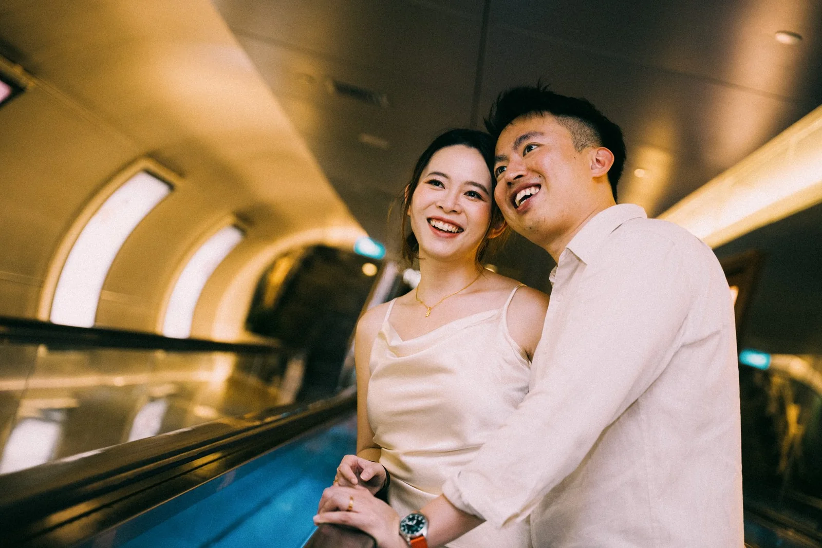 Wee Hung and Ler laughing together in warm light on an escalator